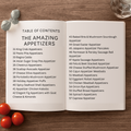 Open book with a table of contents for appetizers on a wooden surface with cherry tomatoes and a glass.